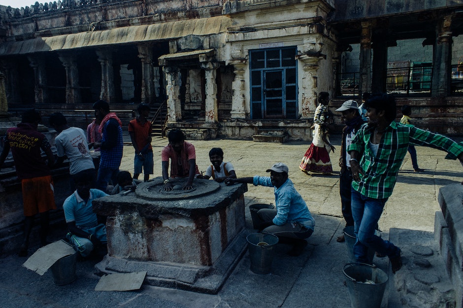 Asian people in casual clothes standing near and touching weathered religious stone wheel located in